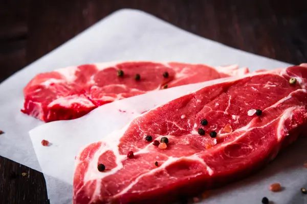 Pedaço de carne crua em papel branco com pimenta — Fotografia de Stock