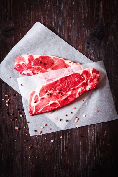 Pezzo di carne cruda su carta bianca con pepe — Foto Stock