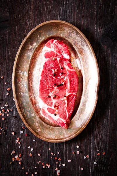Шматок сирої м'ясної яловичини на тарілці з перцем — стокове фото
