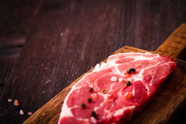 Pezzo di carne cruda di manzo su una tavola di legno con pepe — Foto Stock
