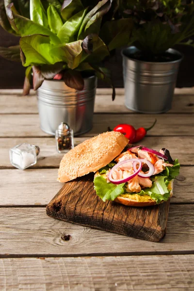 Bagel com alface e salmão assado em uma tábua de madeira , — Fotografia de Stock