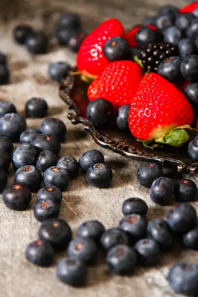 Blueberries and strawberries on a plate and stone background — Stock Photo, Image