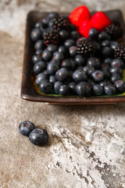 Blaubeeren und Erdbeeren auf einem Teller und Steinhintergrund — Stockfoto