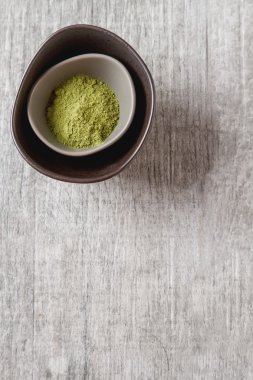 Matcha çay bir küçük kahverengi plaka kuru. Gri ahşap arka plan. Sayfanın Üstü