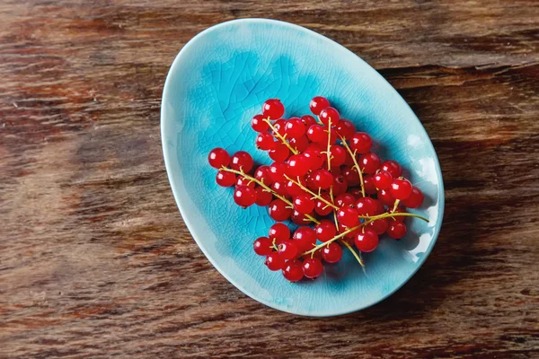 Red ripe currant on a blue plate. Dark wood background. Top view — Stock Photo, Image