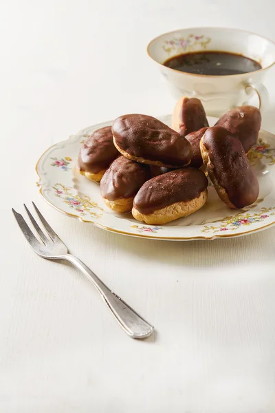 Bolo de chocolate francês, eclairs com uma xícara de café preto quente em — Fotografia de Stock