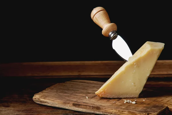 Pedaço de queijo parmesão italiano com uma faca. Backgro de madeira escura — Fotografia de Stock