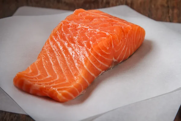 Un trozo de salmón fresco sobre papel de hornear blanco. Espalda de madera oscura — Foto de Stock