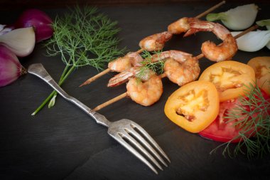 Grilled shrimp with dill tomatoes and onions on a black stone