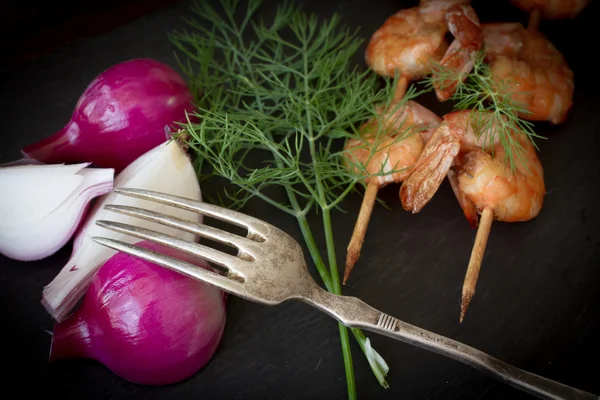Grilled shrimp with dill tomatoes and onions on a black stone — Stok fotoğraf