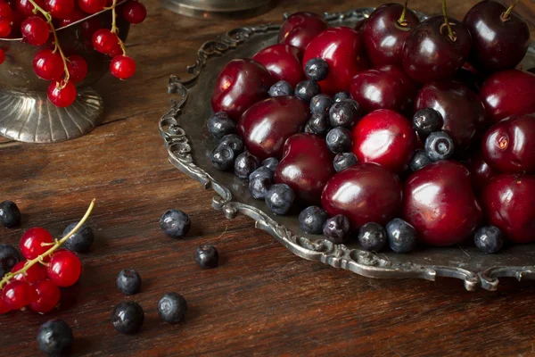 Cereza con grosellas rojas y arándanos en una jarra y un pl de metal —  Fotos de Stock