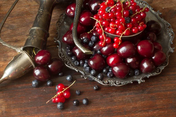 Cereza con grosellas rojas y arándanos en una jarra y un pl de metal —  Fotos de Stock