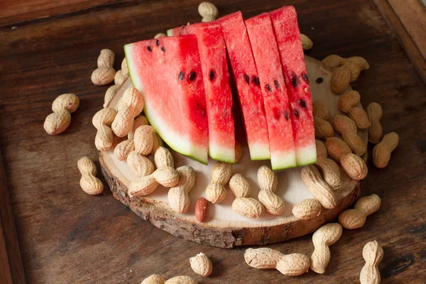 Reife rote Wassermelone mit Erdnüssen auf Holzgrund — Stockfoto