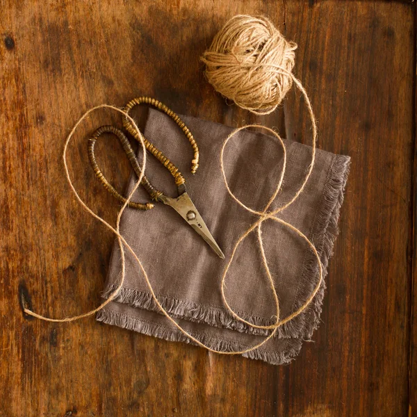 Tijeras acostadas sobre tela de lino con una cuerda sobre un fondo de madera — Foto de Stock