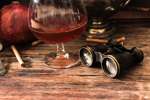 Glass of cognac with binoculars and blue stained-glass candle — Stock Photo, Image