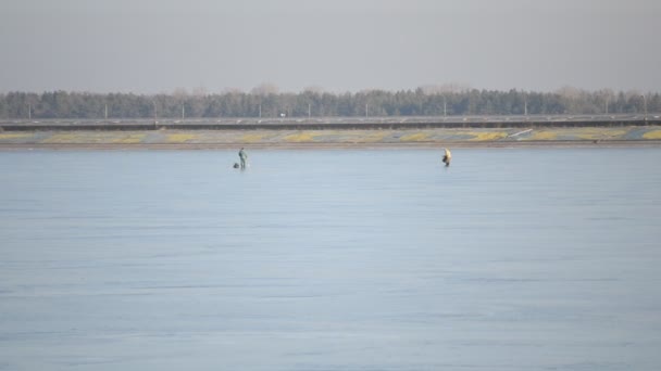 Два зимних рыбака ходят по водохранилищу с замерзшей водой — стоковое видео