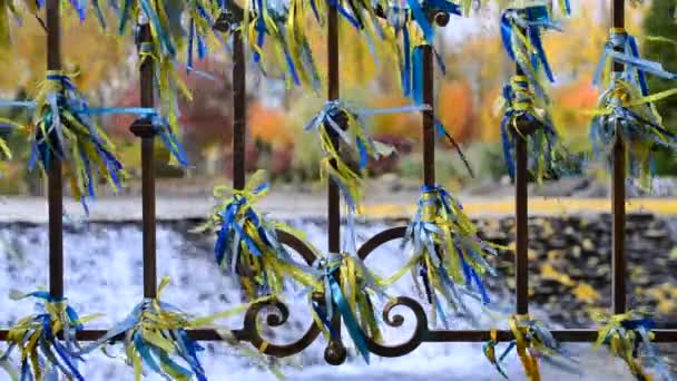 Blauwe en gele linten gebonden aan een ijzeren hek geblazen door de wind — Stockvideo