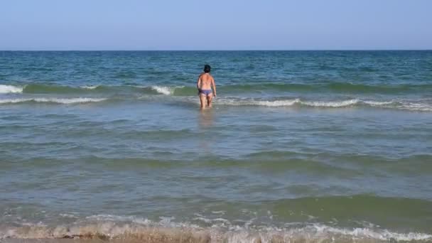 Νεαρή λεπτή γυναίκα με μαγιό πηγαίνει στο νερό της θάλασσας — Αρχείο Βίντεο