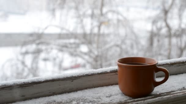 Cup of coffee on old window sill on background of falling snow — Stock Video