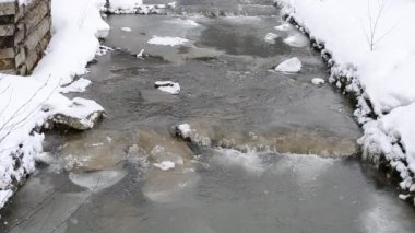 Küçük dağ nehrinin arka planında güzelce yağan kar