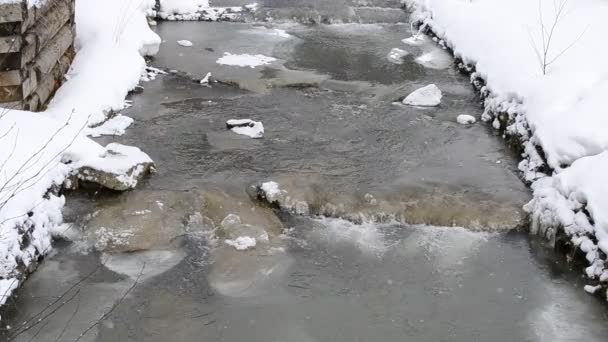 Снег красиво падает на фоне маленькой горной реки — стоковое видео