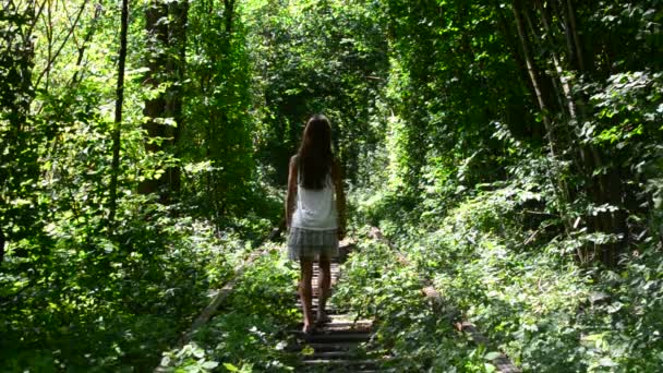 Adolescente marche sur le chemin de fer pittoresque avec des arbres verts autour — Video