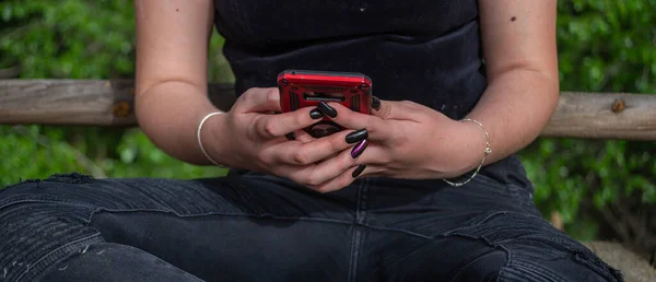 closeup of woman hands with black nails touching mobile phone screen on wooden background