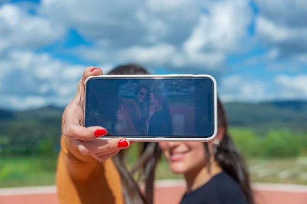 Attractive girl with long hair and orange t-shirt, takes a selfie, with the blue sky in the background, technology and nature concept