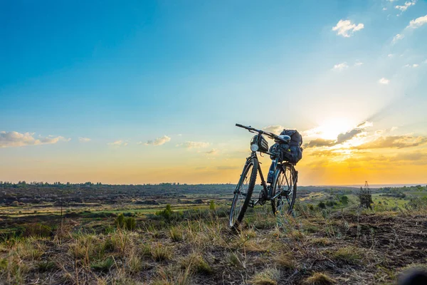 Günbatımı gökyüzünün arka planında bir tepede duran bir bisiklet, arka planda bir vadiyle.