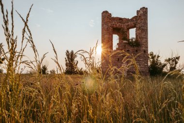 Yaz günü gün batımında bir tarlada bir kulenin yıkıntıları.