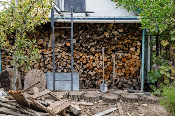 Arka bahçesinde düzgün istiflenmiş yakacak odunları ve yakında duran aletleri var.