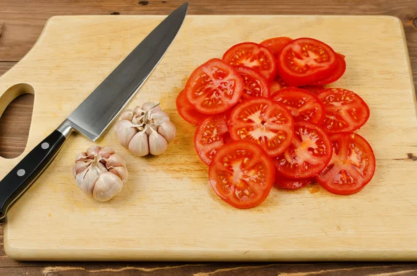 Röd tomat skivor, vitlök och kniv på skärbräda — Stockfoto