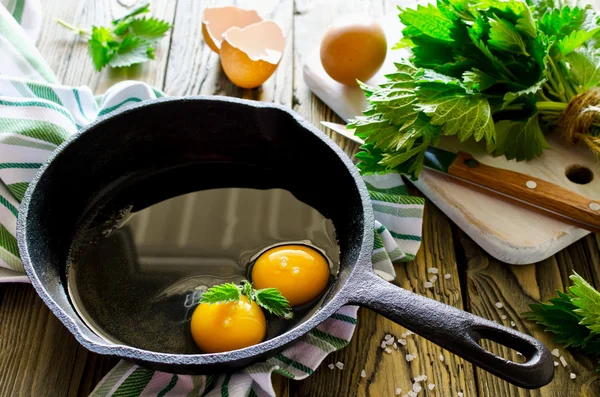 Míchaná vejce s kopřivami v pánvi na dřevěný stůl — Stock fotografie