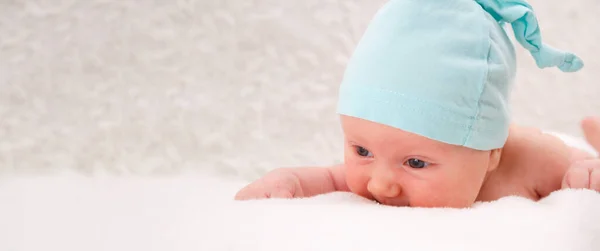Miesięczne dziecko w niebieskiej czapce leży na brzuchu i patrzy na świat. Koncepcja rodziny. Makieta na nagłówku. Copycpace — Zdjęcie stockowe