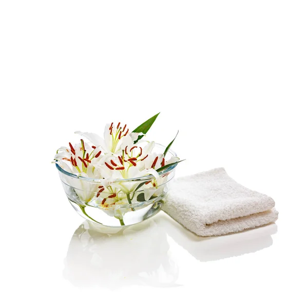 Vaso transparente com água e lírios brancos com uma toalha branca. Isolado em branco. Conceito de spa para limpeza, frescura e aromaterapia. — Fotografia de Stock