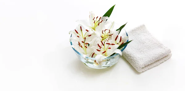 Jarrón transparente con agua y lirios blancos con una toalla blanca. Aislado sobre blanco. Concepto de spa para limpieza, frescura y aromaterapia. — Foto de Stock