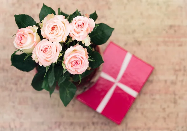 Vase with roses and gift with ribbon — Stock Photo, Image