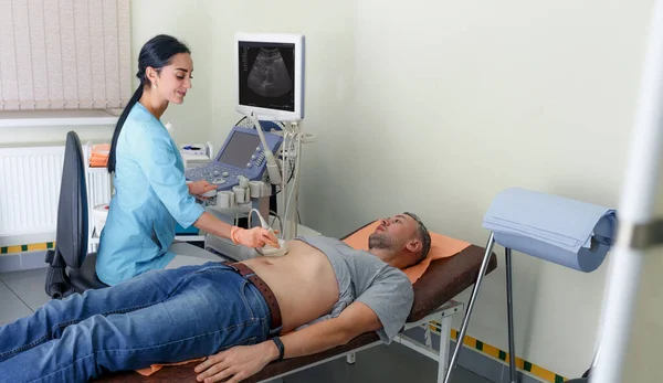 A young girl doctor makes an examination of the abdominal cavity on an ultrasound machine in a male patient.