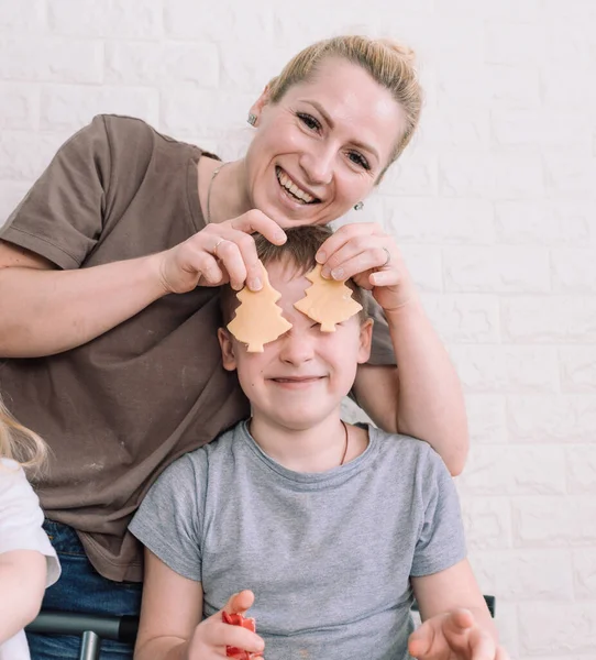 happy mom and her son play together while making cookies in the kitchen. mom covers baby s eyes with freshly made cookies