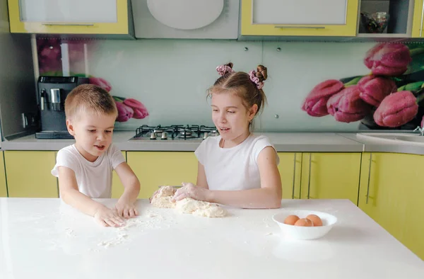 beautiful boy and girl stretching dough in the kitchen are messing around and having fun while cooking. happy happy children