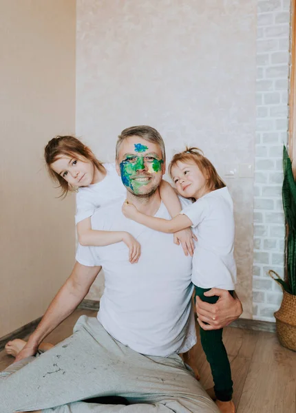 a happy dad with a painted face embraces two loving daughters. father\'s day