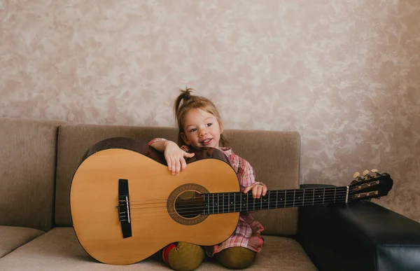 a little beautiful girl learns to play the guitar sitting at home on the couch. learning music