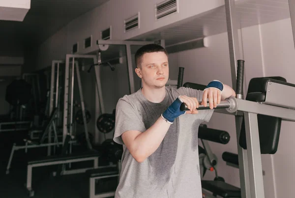 a portrait of a tired athlete in a wet T-shirt stands near the simulator. rest after an intense workout