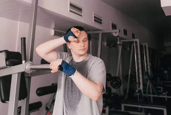 a portrait of a tired athlete in a wet T-shirt stands near the simulator. rest after an intense workout