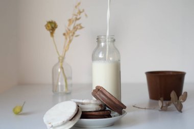 vertiendo leche en una botella, al lado una pila de alfajores de chocolate argentinos 