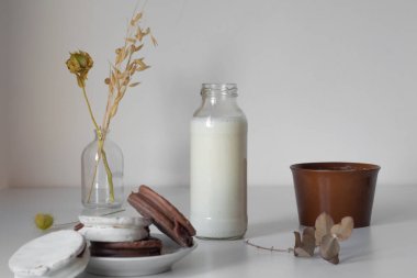 botella de leche de vaca, sobre una mesa blanca y al lado tiene azucar y alfajores de chocolate argentinos