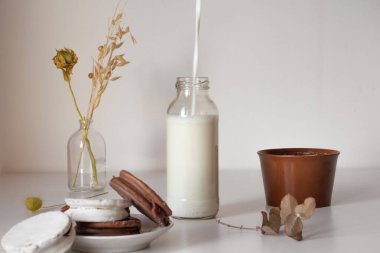 botella de leche de vaca, sobre una mesa blanca, alfajores de chocolate argentinos en un plato blanco