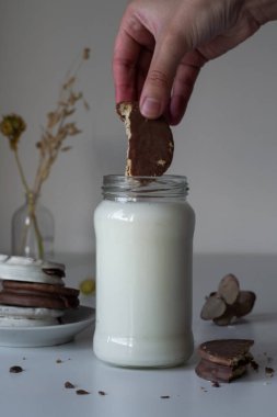 untando un alfajor de çikolata negro, en un vaso de leche