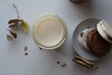 Vaso de leche visto desde arriba, al lado un plato lleno de alfajores cubiertos de un delicioso çikolatası