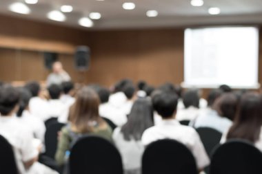 Öğretmen ve beyaz projektör ekranı önünde oturan üniversite öğrencilerinin bulanık arkaplanı